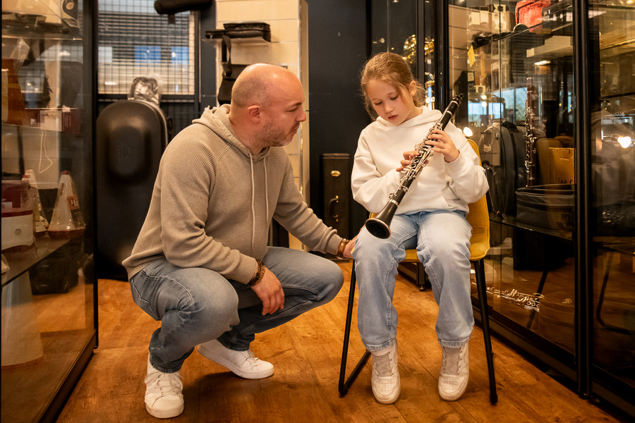 Jonge muzikant probeert een klarinet met uitleg van een medewerker